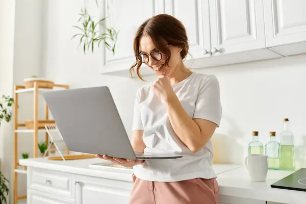 Middle aged woman uses laptop in kitchen. — Stock Photo