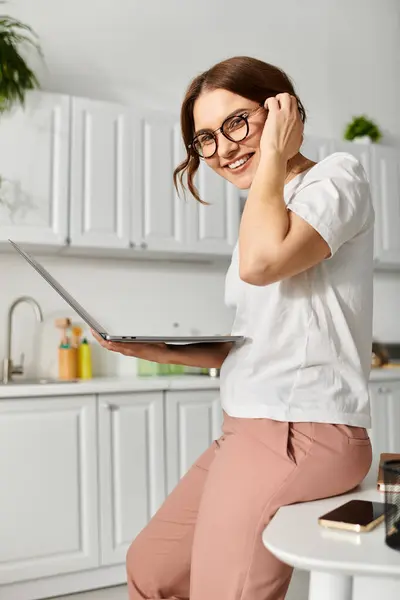 Middle-aged woman sitting on table, working on laptop. — Stock Photo
