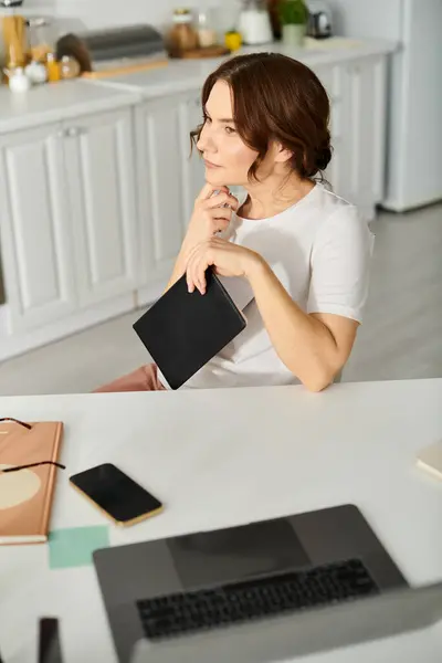 Middle-aged woman sitting at kitchen table, using a tablet. — Stock Photo