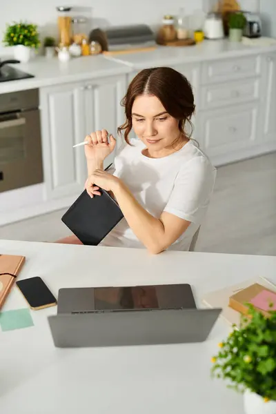 Frau mittleren Alters sitzt am Küchentisch und arbeitet am Laptop. — Stockfoto