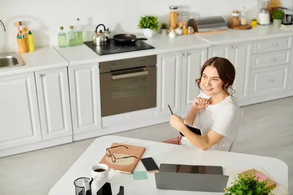 Eine Frau mittleren Alters sitzt an einem Küchentisch, eingetaucht in einen Moment der Ruhe und Kreativität. — Stockfoto
