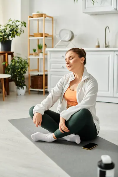Mujer de mediana edad meditando pacíficamente en la esterilla de yoga en la habitación. - foto de stock
