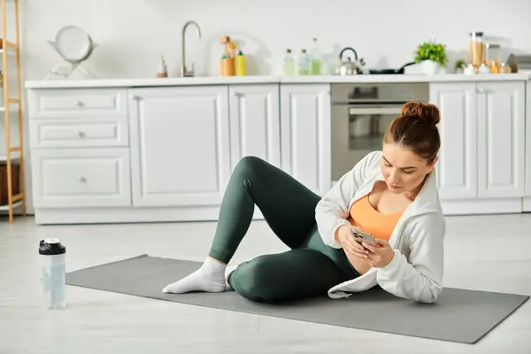 Frau mittleren Alters sitzt auf Yogamatte und wird vom Smartphone-Bildschirm gefesselt. — Stockfoto