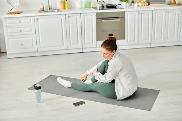 Mulher de meia-idade encontrar paz interior em um tapete de ioga em sua cozinha. — Fotografia de Stock