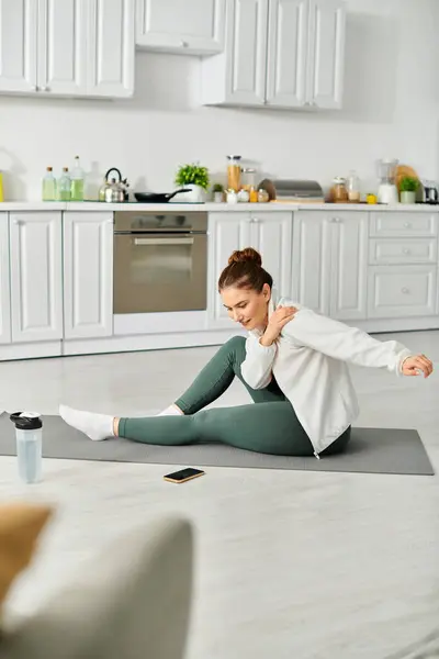 Mujer de mediana edad practica con gracia yoga en una estera en la cocina. - foto de stock