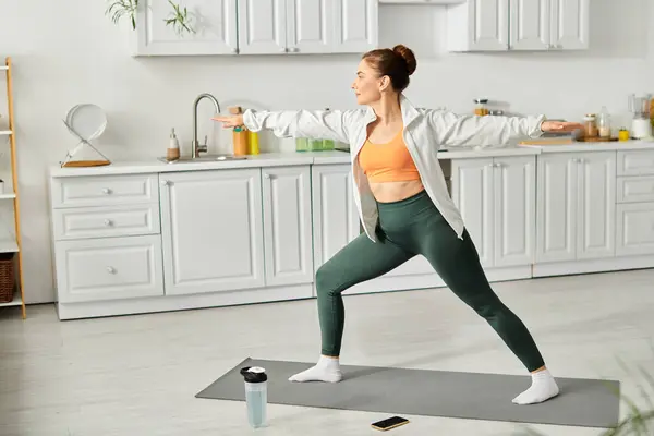 Mujer de mediana edad golpea elegantemente postura de yoga en su cocina. - foto de stock