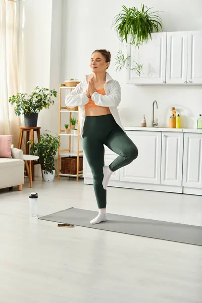 Femme d'âge moyen en chemise blanche faisant gracieusement du yoga à la maison. — Photo de stock