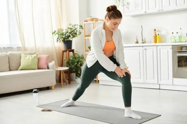 Mujer de mediana edad con gracia sostiene una pose de yoga en una alfombra en casa. - foto de stock
