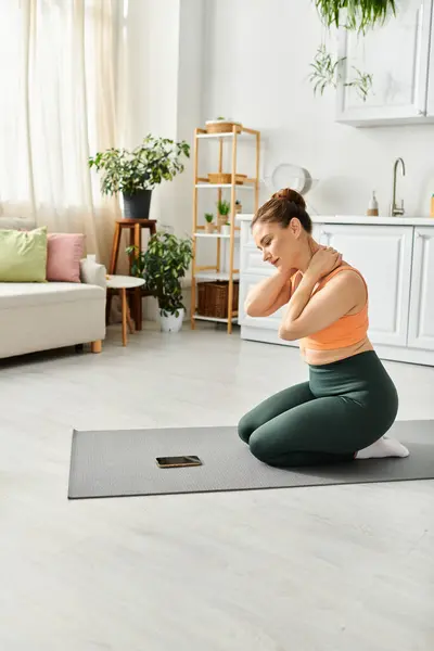 Femme d'âge moyen pratiquant paisiblement le yoga sur un tapis confortable dans son salon à la maison. — Photo de stock