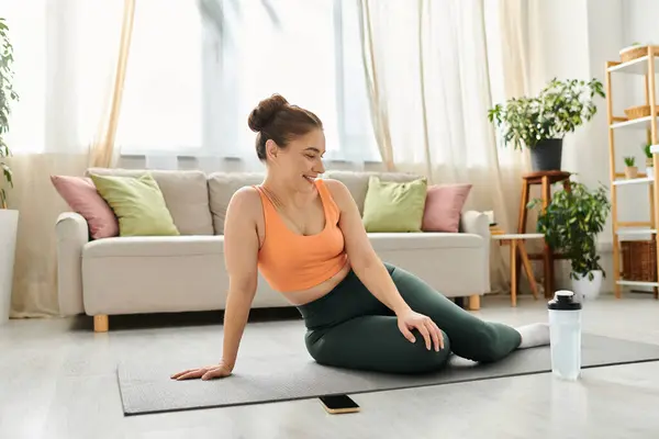 Femme d'âge moyen est assis paisiblement sur tapis de yoga dans un cadre détendu à la maison. — Photo de stock