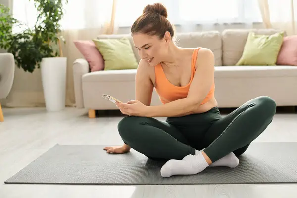 Donna di mezza età si siede su tappetino yoga, assorbito nel telefono. — Foto stock
