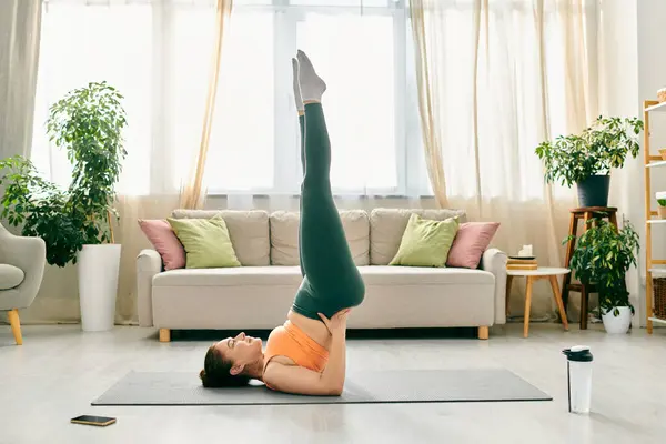 Middle-aged woman performing a handstand in her living room. — Stock Photo