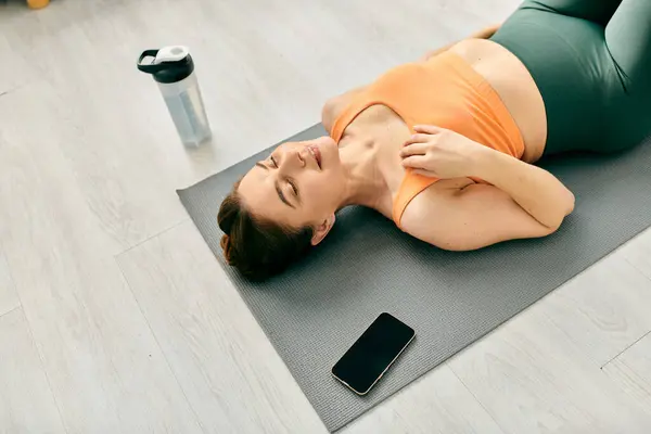 Mujer de mediana edad acostada en una esterilla de yoga, usando un teléfono celular. - foto de stock