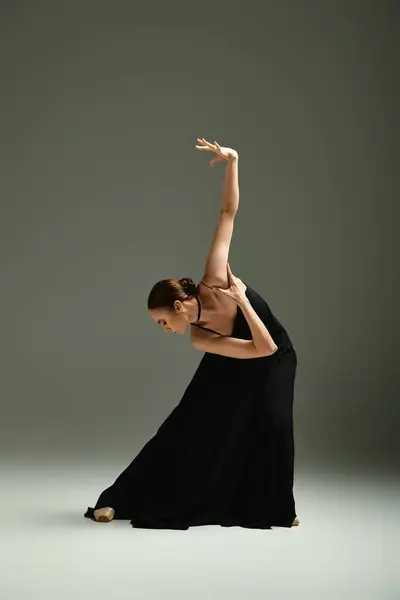 Молода, красива балерина в чорній сукні вражає танцювальну позу з грацією і майстерністю. — стокове фото