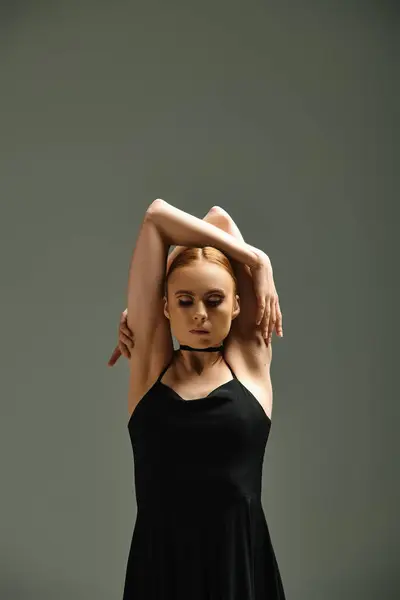 Una hermosa bailarina joven en un vestido negro posa con las manos en la cabeza. - foto de stock