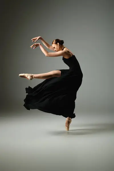 Eine junge, schöne Ballerina tanzt anmutig in einem fließenden schwarzen Kleid. — Stockfoto