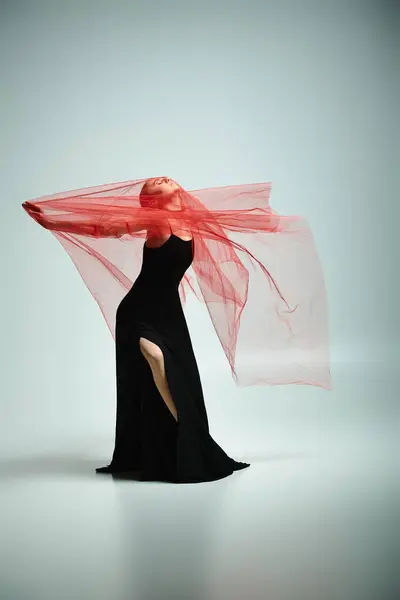 Una bailarina joven y talentosa baila elegantemente en un vestido negro con un llamativo velo rojo. - foto de stock