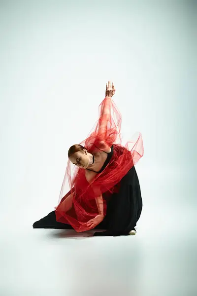 Грациозная балерина с красной вуалью танцует на земле — стоковое фото