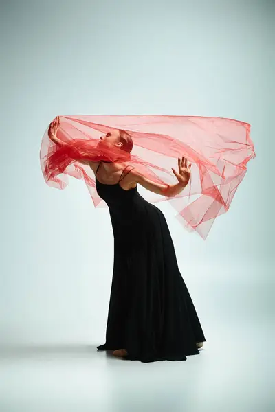 A young beautiful ballerina in a flowing black dress and vibrant red scarf dances gracefully. — Stock Photo