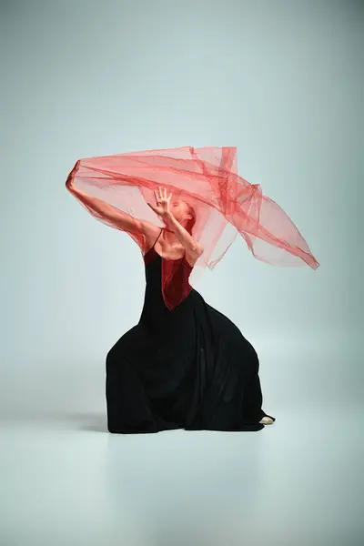 Uma bailarina graciosa em um vestido preto impressionante se move elegantemente com um véu vermelho na cabeça. — Fotografia de Stock