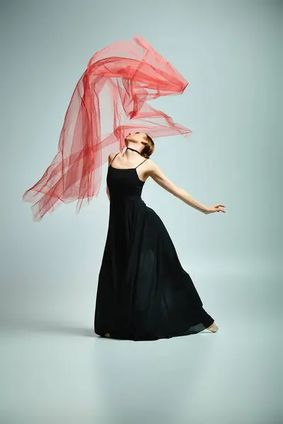 Молода балерина в чорній сукні і червоний шарф демонструє талант і красу через витончений танець. — стокове фото