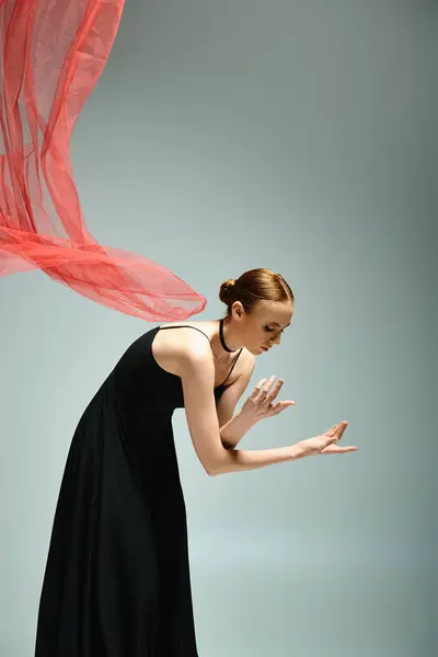 Uma bailarina jovem e bonita dança graciosamente em um vestido preto e um xale vermelho vibrante.. — Fotografia de Stock
