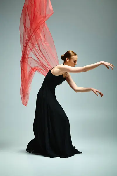 Una joven y hermosa bailarina en un vestido negro se mueve con elegancia con un velo rojo. — Stock Photo