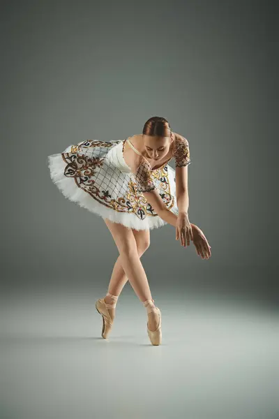 Eine junge Ballerina im weißen Tutu tanzt anmutig vor grauem Hintergrund. — Stock Photo