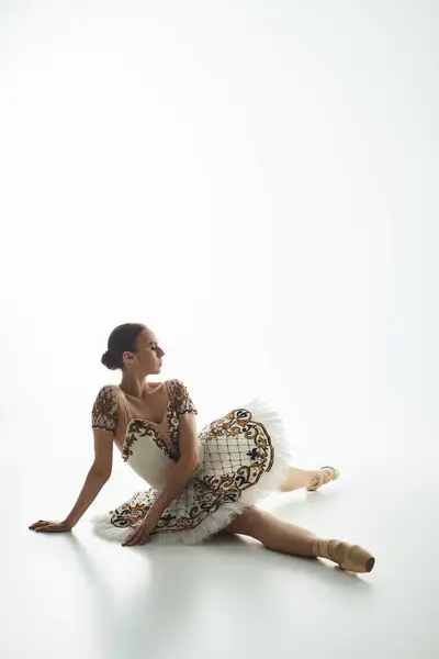 Uma bailarina jovem e bonita em um vestido se senta graciosamente no chão. — Fotografia de Stock