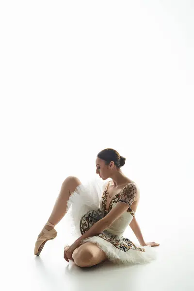 A young beautiful ballerina sits on the floor with crossed legs. — Stock Photo