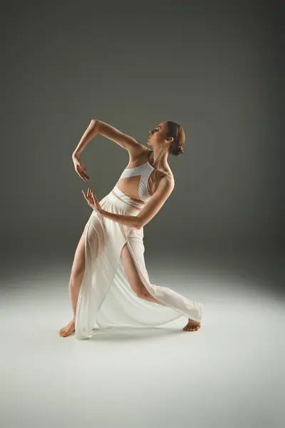 Una bailarina elegante en un vestido blanco que fluye golpeando una pose. - foto de stock