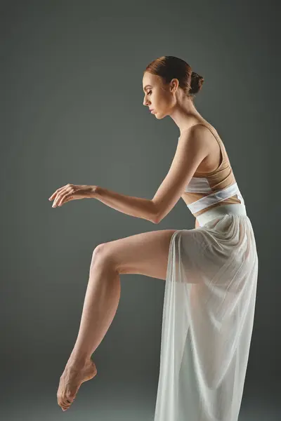 Una talentosa bailarina joven da una pose elegante en un vestido blanco que fluye. - foto de stock