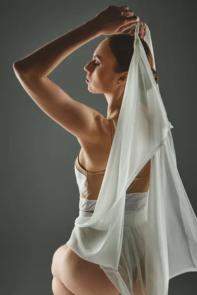 Una giovane donna con un vestito bianco regge con grazia una sciarpa bianca sopra la testa. — Foto stock