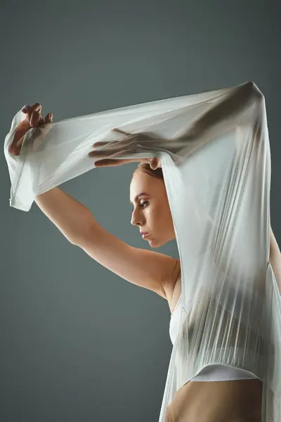 A young ballerina in a white dress gracefully holds her veil over her head. — Stock Photo