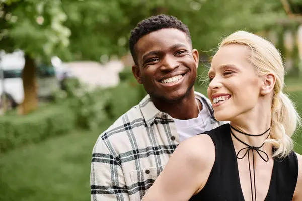 A joyful multicultural couple smiling brightly in a sunlit park setting. — Stock Photo
