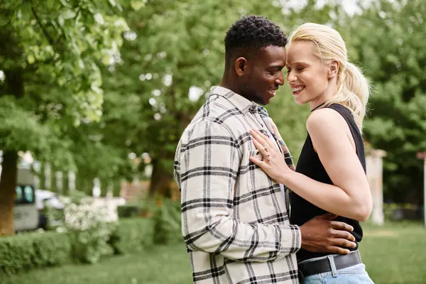 Un homme afro-américain heureux et une femme caucasienne se tenant étroitement ensemble dans un parc animé, mettant en valeur l'amour et l'unité. — Photo de stock