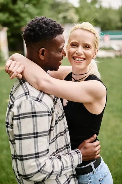 Ein glückliches Paar, bestehend aus einem afroamerikanischen Mann und einer kaukasischen Frau, das sich inmitten eines lebhaften Parks liebevoll umarmt. — Stockfoto