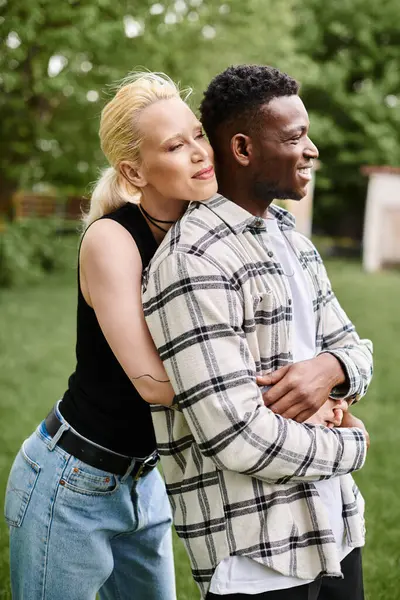 A multicultural couple, an African American man and a Caucasian woman, share a warm embrace amidst lush greenery in the park. — Stock Photo