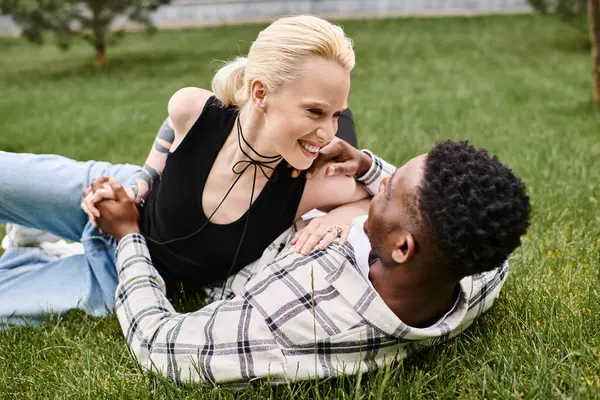 A happy multicultural couple, an African American man and a Caucasian woman, relaxing together in the lush green grass of a park. — Stock Photo