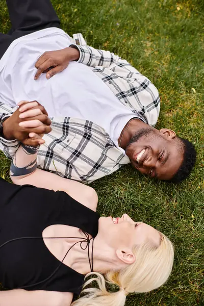Un uomo afroamericano e una donna caucasica sono distesi sull'erba, abbracciandosi con il sorriso in faccia. — Foto stock
