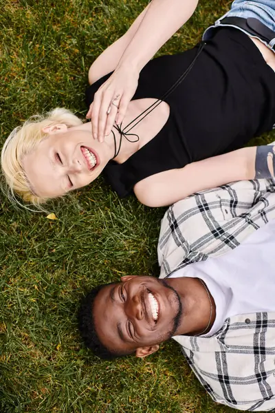A joyful African American man and Caucasian woman lying together on the green grass, connecting in the peaceful outdoor setting. — Stock Photo