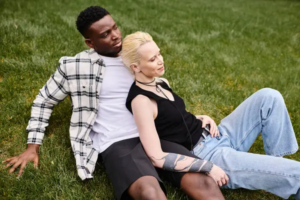 A multicultural couple, an African American man, and a Caucasian woman, laying contently on the grass in a park. — Stock Photo