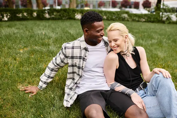 Um casal feliz, multicultural, composto por um homem afro-americano e uma mulher caucasiana, sentado na grama em um parque. — Fotografia de Stock