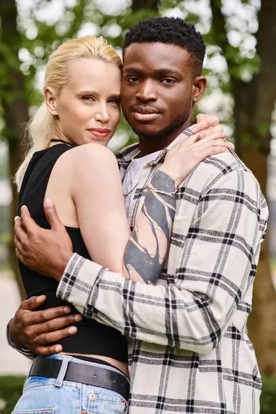 Un momento de alegría en un parque como una pareja multicultural, un hombre afroamericano y una mujer caucásica, se abrazan. - foto de stock