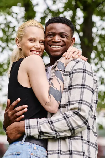 Una pareja feliz y multicultural, un hombre negro y una mujer caucásica, se abrazan amorosamente en un entorno de parque. - foto de stock