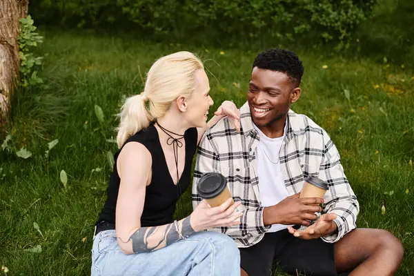 A happy multicultural couple, an African American man and a Caucasian woman, sitting together on the grass in a park. — Stock Photo