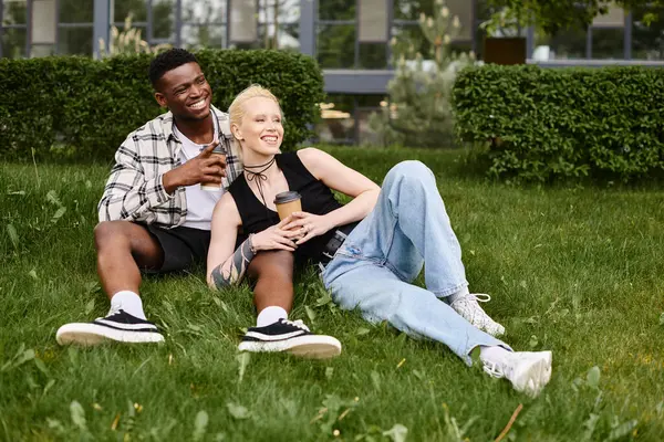 Африканський американець і кавказька жінка сидять разом на зеленій траві в парку, насолоджуючись мирною миттю на відкритому повітрі. — стокове фото