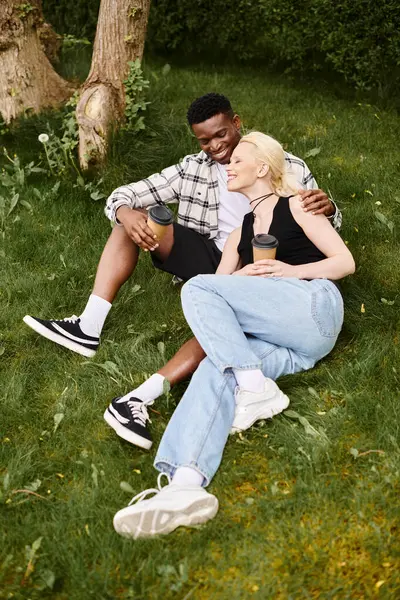 A content African American man and Caucasian woman sit together on lush green grass, enjoying a peaceful moment outdoors. — Stock Photo
