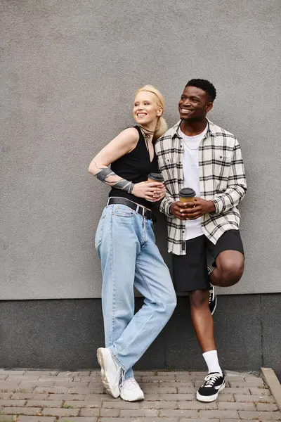 Una pareja feliz, un novio y una novia multiculturales, parados uno al lado del otro en una calle urbana cerca de un edificio gris. - foto de stock