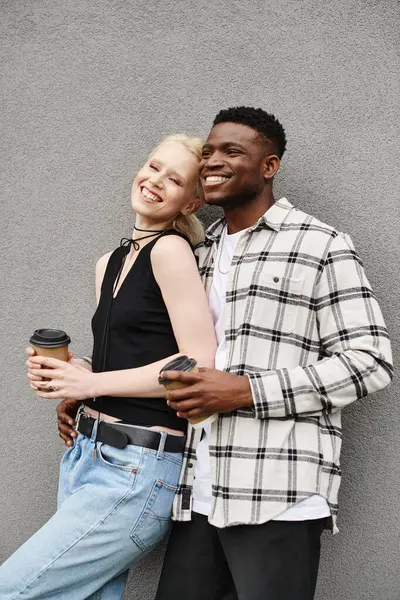 A happy multicultural couple stands side by side on an urban street near a grey building. — Stock Photo